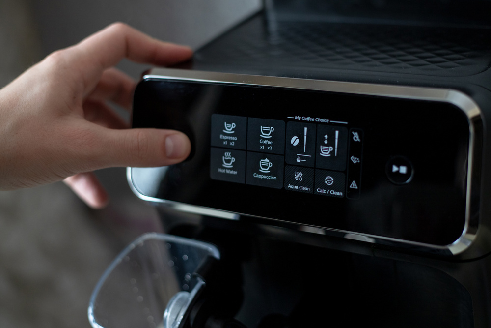 A man's hand presses the power button of a black coffee machine