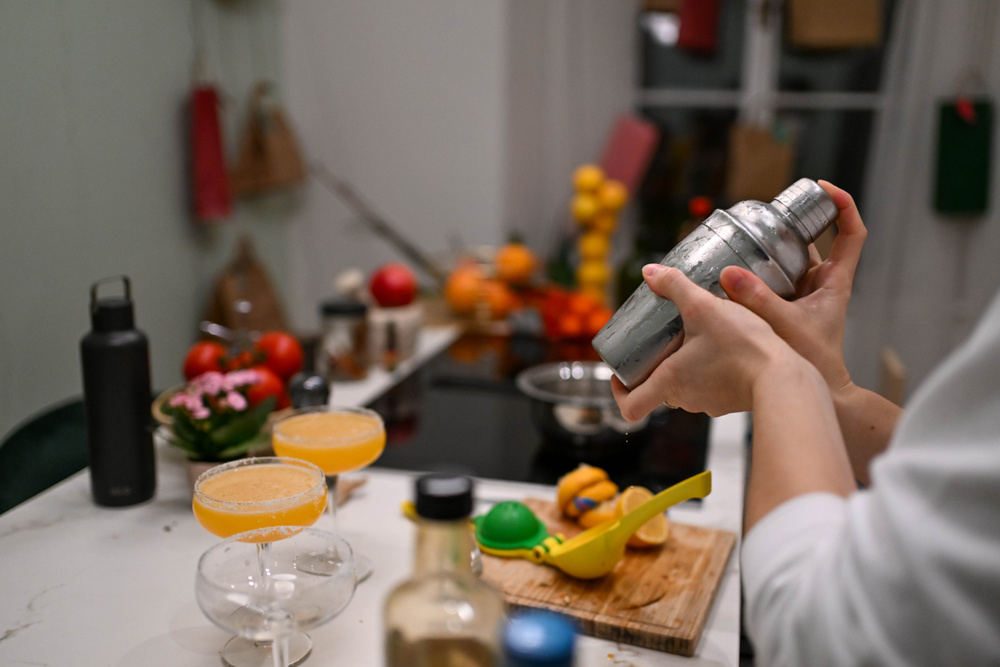 A person is shaking a stainless steel cocktail shaker over a white countertop