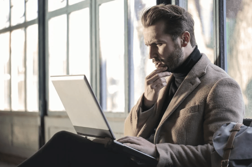 A man looking at his laptop screen and thinking.