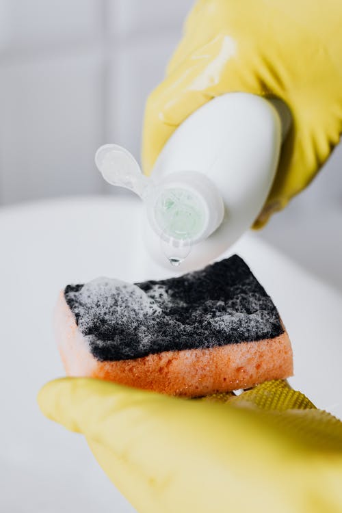 A person pouring detergent on a kitchen sponge.