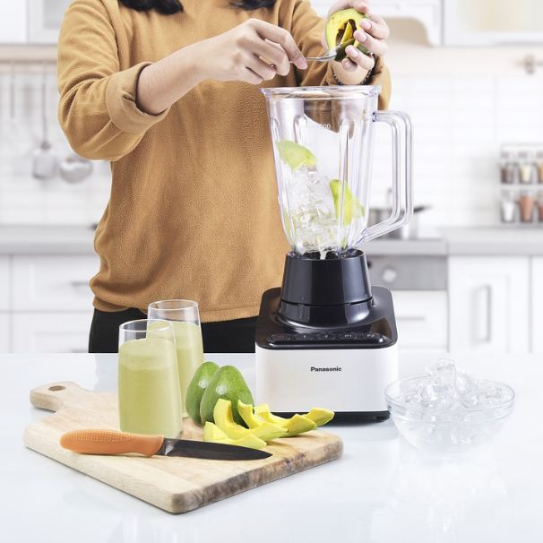 A woman adding avocado to the unblended smoothie