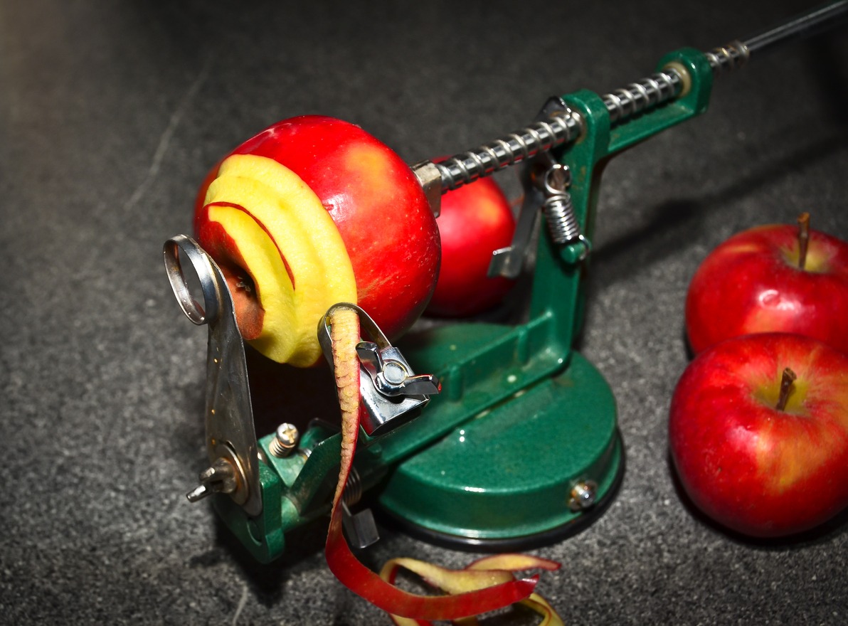 A green mechanical apple peeler peeling red apples