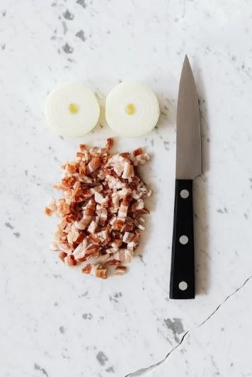 Small paring knife on chopping board next to meat and onions